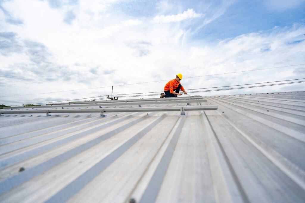 Metal roof worker installing or repairing roof panels on industrial building.